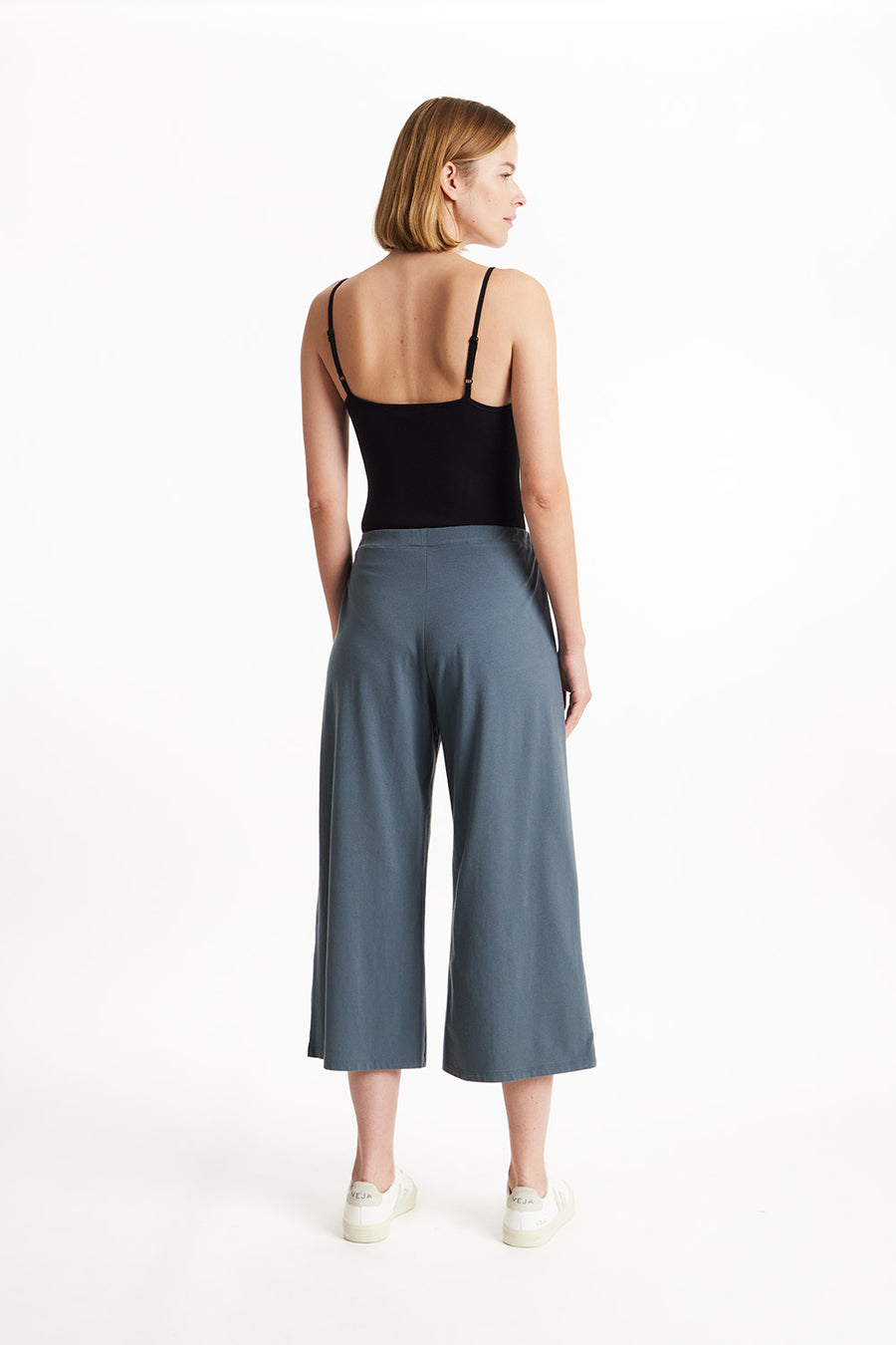 Rear view of a blonde model wearing cropped grey wide leg Chandre trousers by People Tree over a black bodysuit